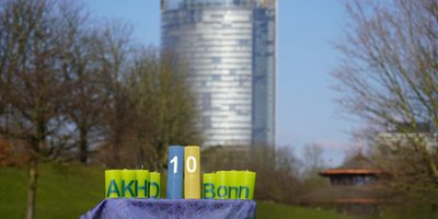 Dieses Foto zeigt die Jubiläumskerzen in der Bonner Rheinaue mit dem Posttower im Hintergrund. Die Kerzen mit der "10" sind in den Farben der Ukraine, Blau und gelb, eingefärbt.